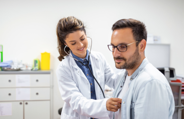 A Man And Woman Stand Before A Doctor In A Medical Office, Discussing Health Concerns.